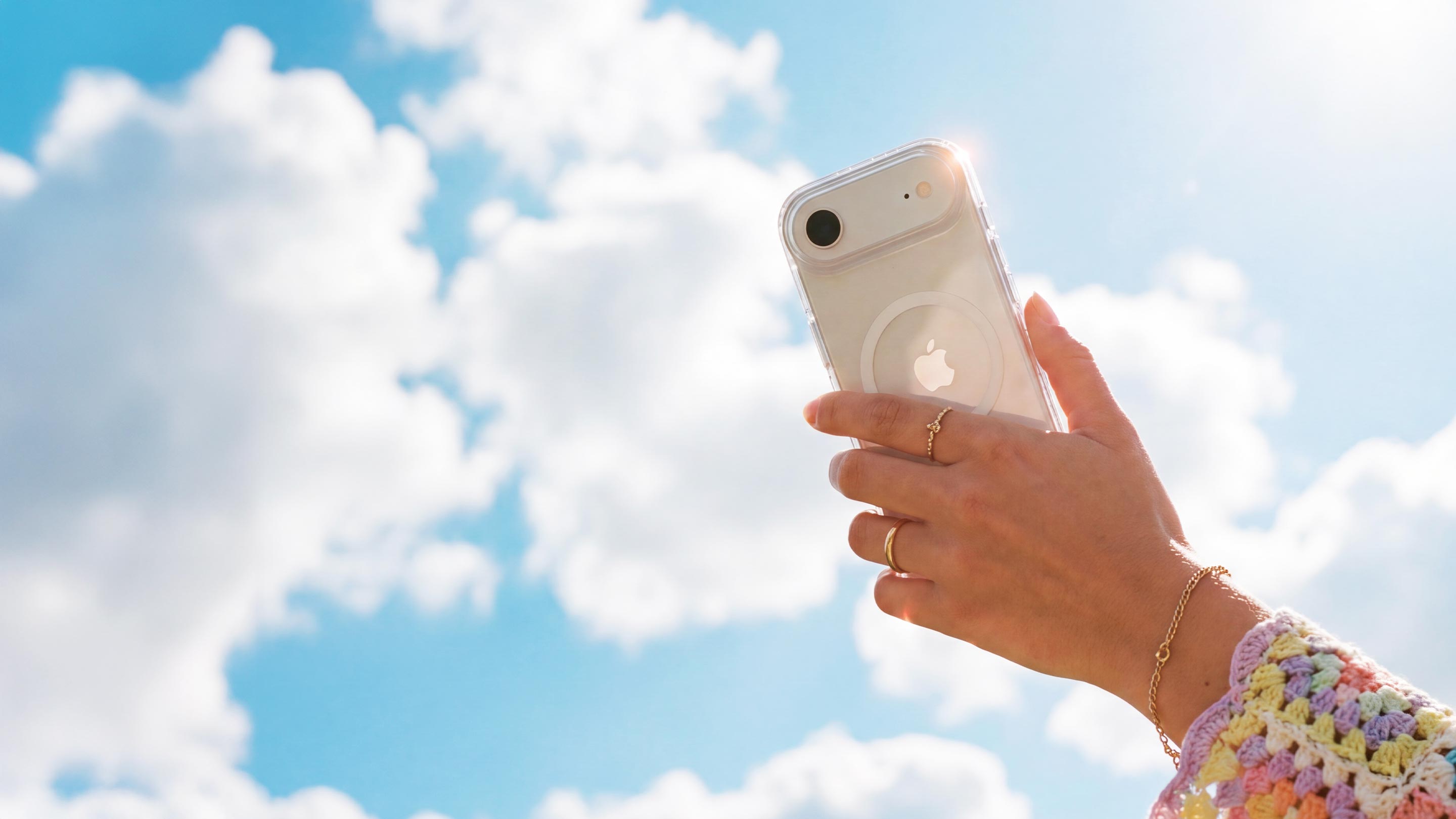 A woman's hand is shown holding an iPhone in a clear case by Tech21 with a blue sky and patchy clouds in the background